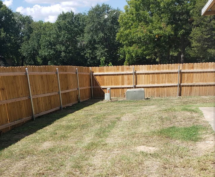 Fenced back yard mowed clean around utility boxes and a wooden fence