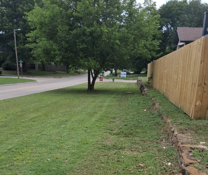 Corner property mowed and trimmed along a fence and stone retaining wall