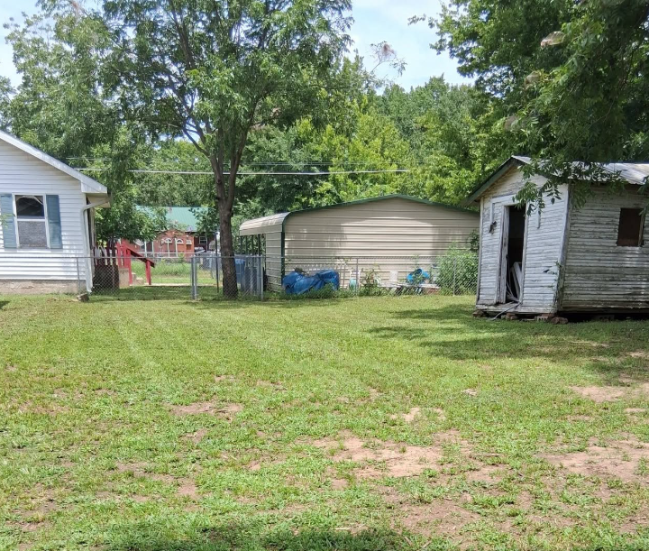 Back yard mowed cleanly between a shed and carport