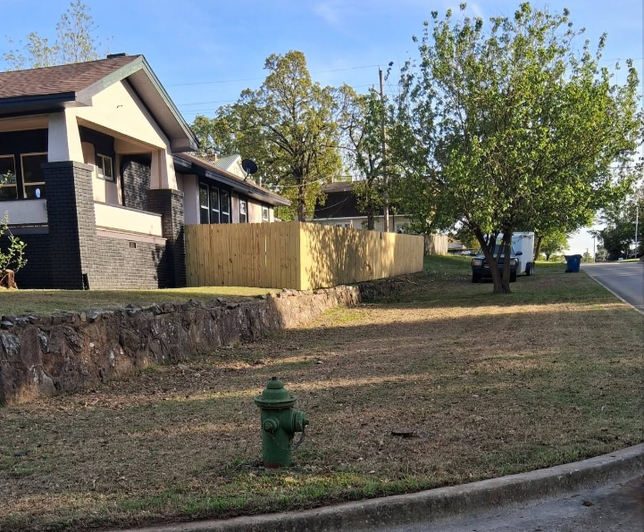 Roadside yard trimmed along a stone retaining wall and new privacy fence