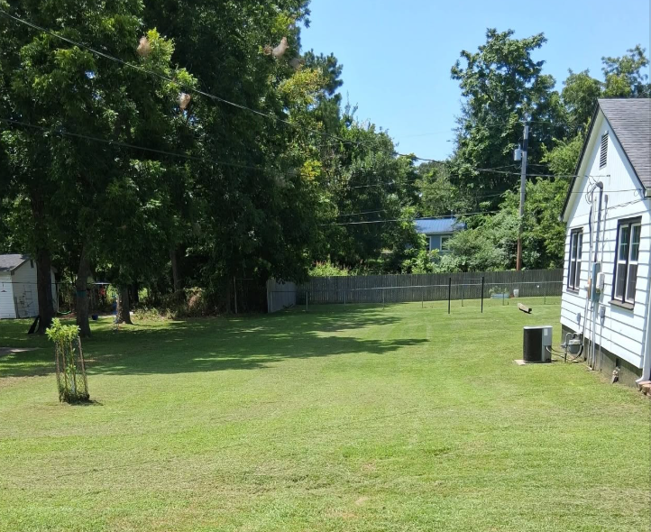 Fenced back yard mowed in clean lines beside a white house