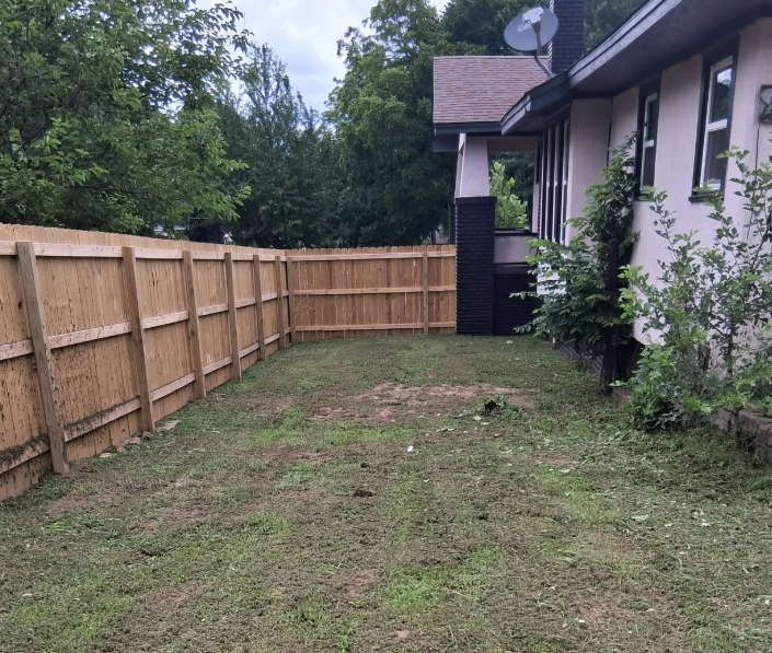 Narrow side yard cleared and mowed between a fence and the house