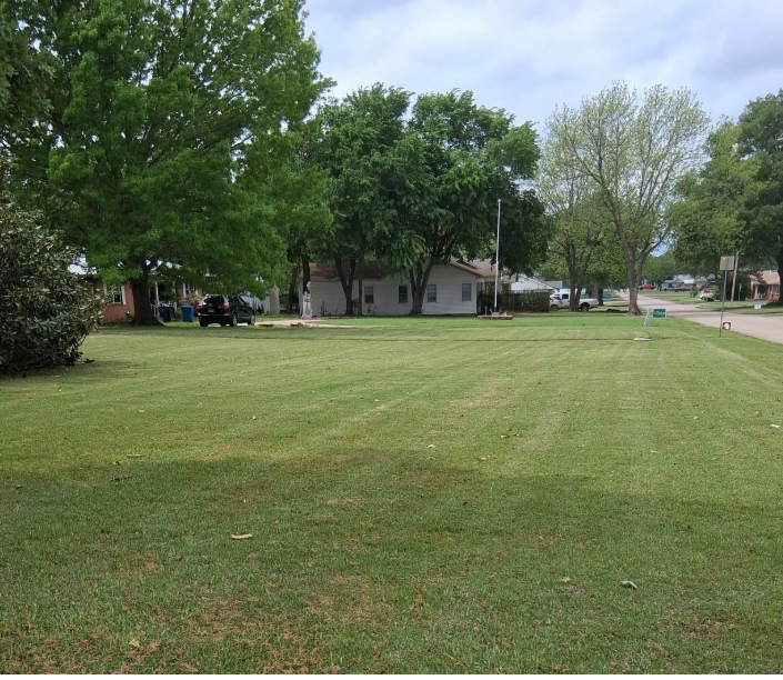Wide corner property mowed in clean stripes along a neighborhood street