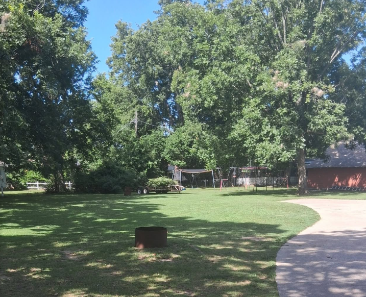 Wide shaded property mowed around mature trees and a play area