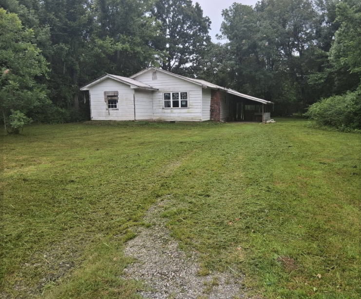 Overgrown rural lot mowed clean around a vacant white farmhouse