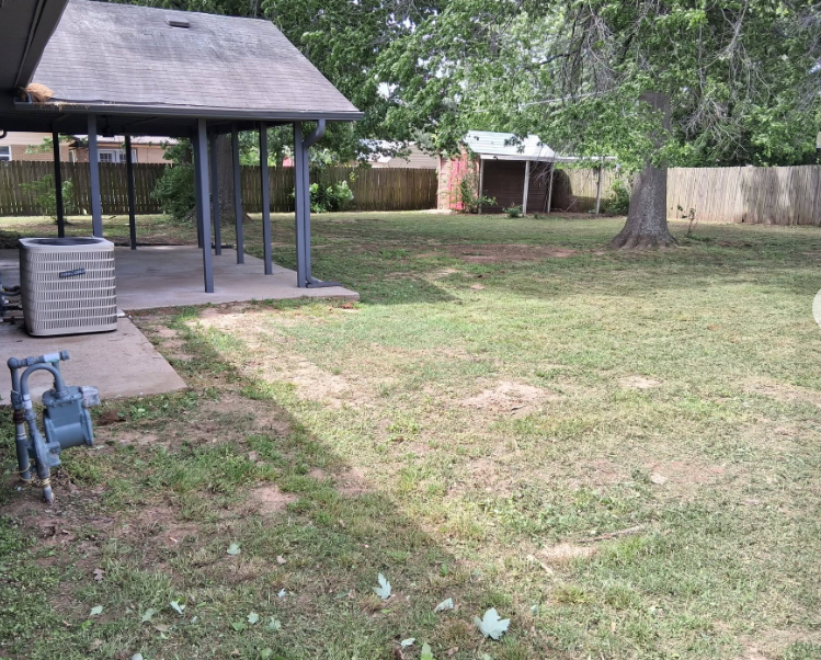 Fenced back yard mowed and trimmed around a covered patio and shade tree