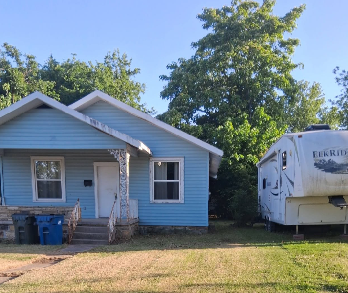 Front yard mowed and trimmed beside a blue house and parked camper