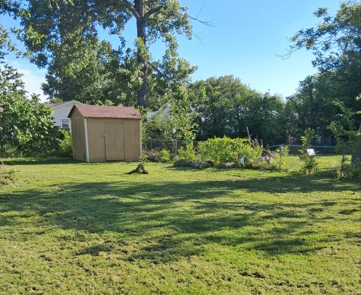 Fenced back yard mowed cleanly around a storage shed and tree line