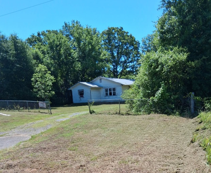 Rural lot mowed inside a chain link fence beside a white farmhouse