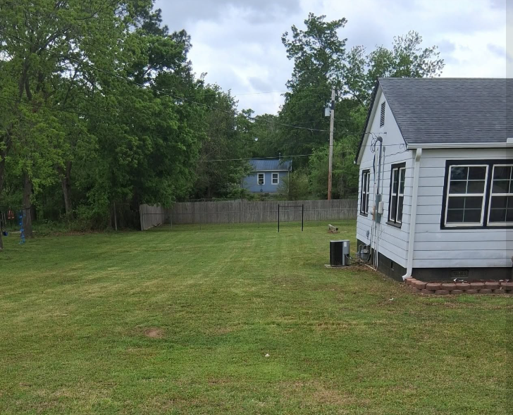 Back yard mowed evenly beside a white house and fence line